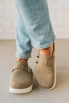 Person wearing beige shoes with buckles and light blue jeans on a neutral background