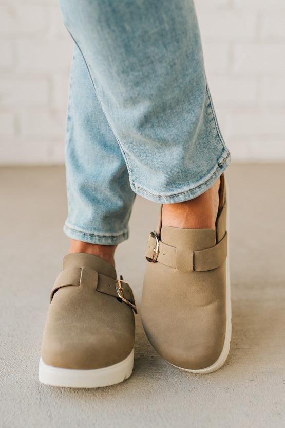Person wearing beige shoes with buckles and light blue jeans on a neutral background