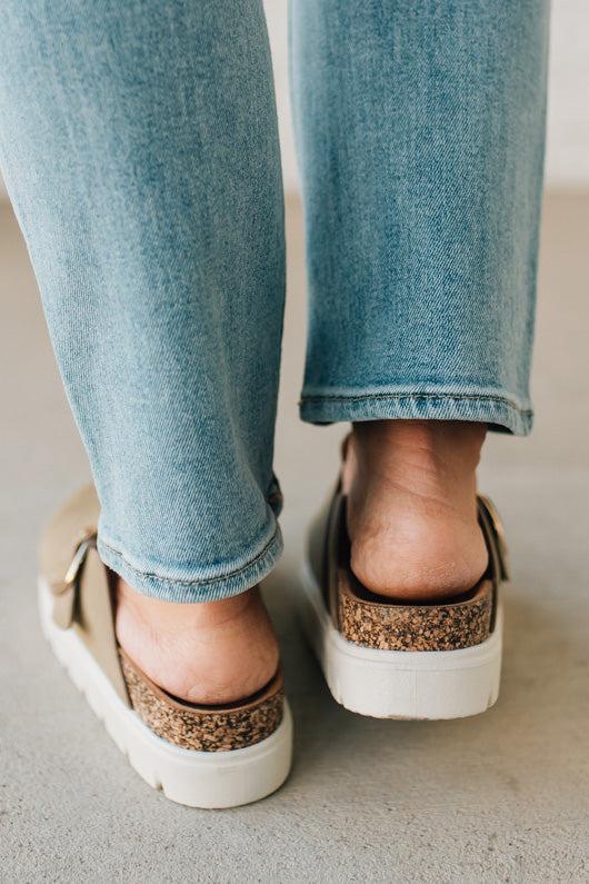Person wearing light blue jeans and cork-sole sneakers on a neutral background