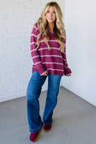 Woman wearing a striped sweater and jeans standing against a white brick wall.