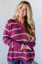 Woman wearing a purple and white striped sweater against a white brick wall.