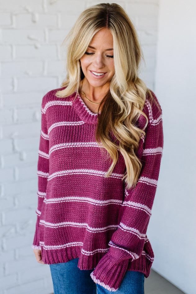 Woman wearing a maroon and white striped sweater against a white brick wall.