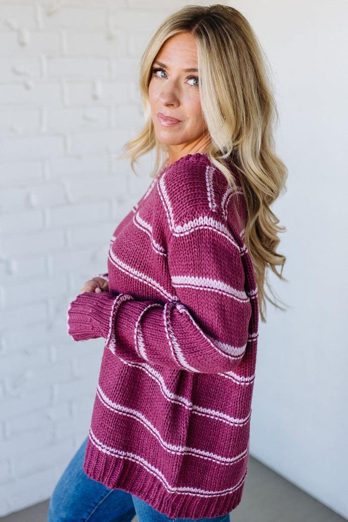 Woman wearing a maroon and white striped sweater against a white brick wall.