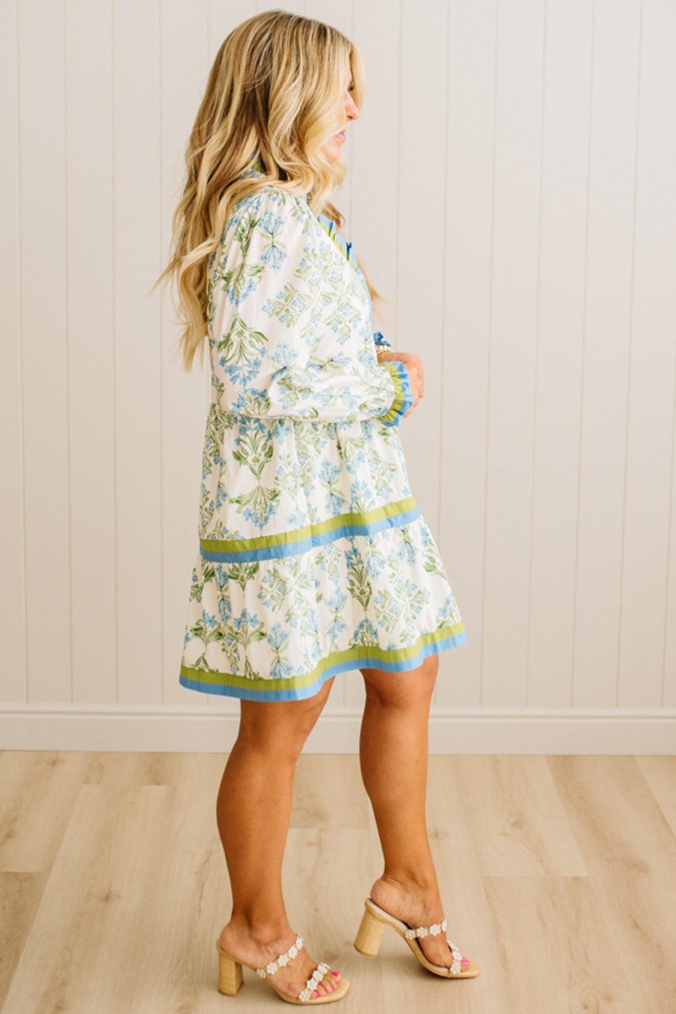 Woman wearing a floral dress standing against a white paneled wall.