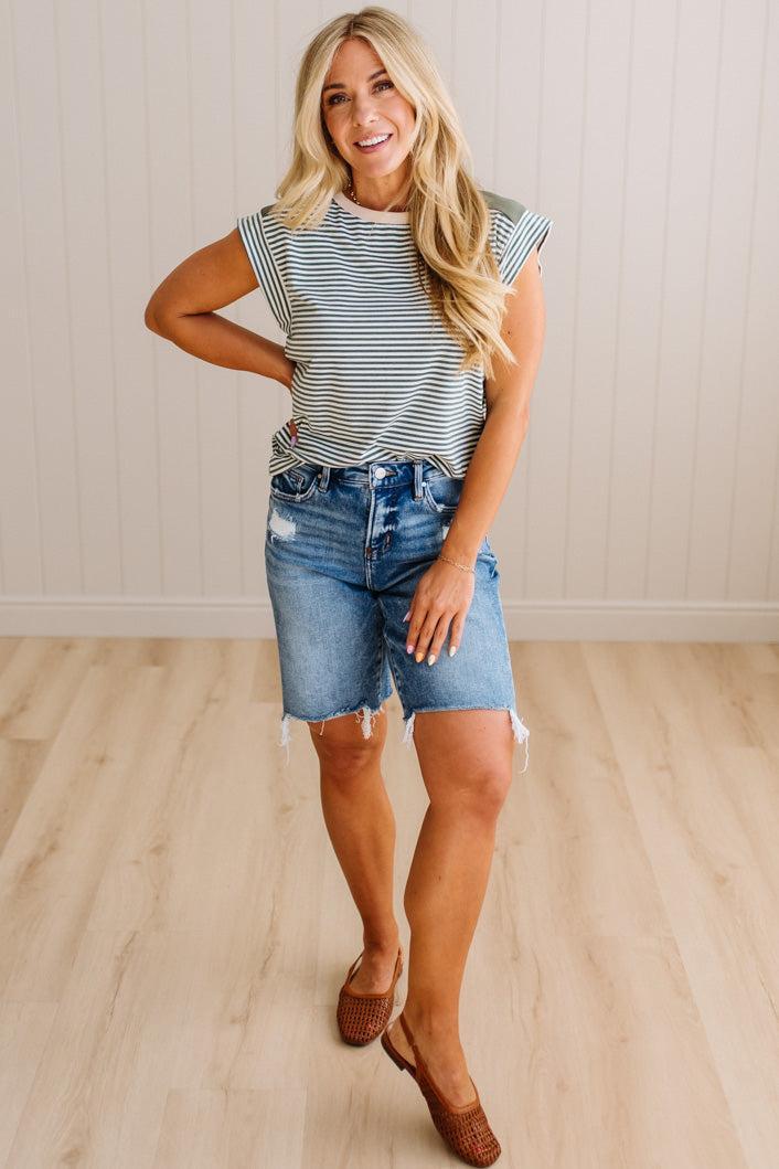 Woman wearing a striped shirt and denim shorts standing on a wooden floor.