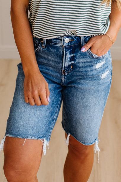Person wearing blue denim shorts and a striped shirt with a neutral background