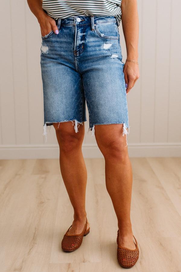 Person wearing blue denim shorts with a striped shirt and brown shoes on a light wooden floor.