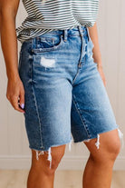 Person wearing a striped shirt and denim shorts with a neutral background