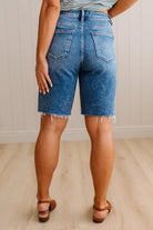 Person wearing blue denim shorts standing on a wooden floor with a neutral background