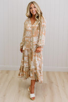 Woman wearing a long, patterned dress standing against a white wall.