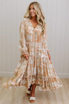 Woman wearing a long, patterned dress standing against a white paneled wall.