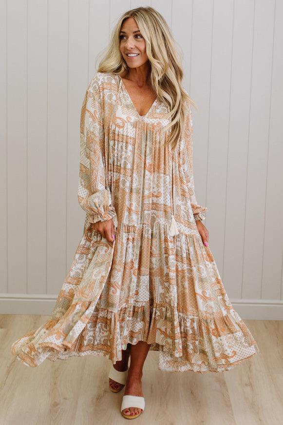 Woman wearing a long, patterned dress standing against a white paneled wall.