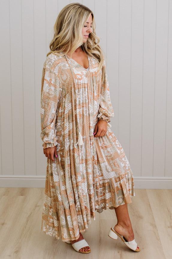Woman wearing a long, patterned dress standing against a white paneled wall.