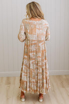 Woman wearing a long, patterned dress against a white paneled wall.