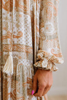 Close-up of a patterned fabric with tassels and ruffles, held by a hand.