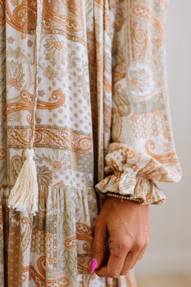 Close-up of a patterned fabric with tassels and ruffles, held by a hand.