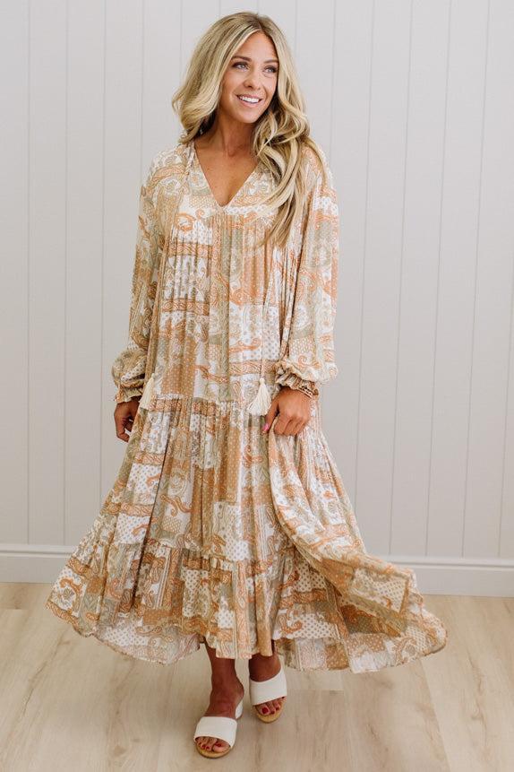 Woman wearing a floral dress standing against a white paneled wall.