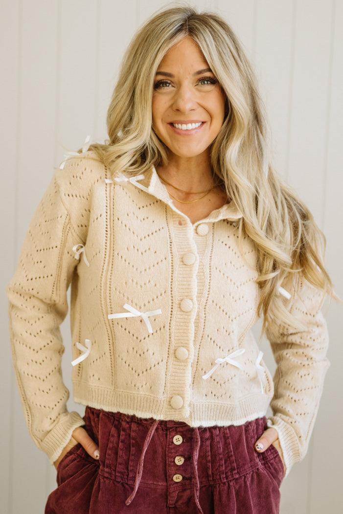Woman wearing a beige knitted cardigan with white buttons against a neutral background