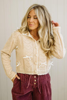 Woman wearing a beige knitted cardigan with white buttons against a neutral background