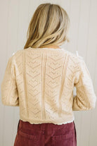 Person wearing a beige knitted cardigan with a subtle pattern against a plain background