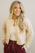 Woman wearing a beige cardigan over a white top and maroon skirt against a neutral background