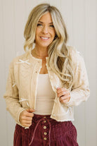 Woman wearing a beige knitted cardigan over a white top and maroon pants against a neutral background