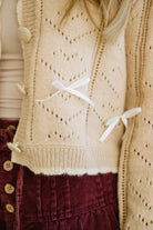 Close-up of a beige knitted vest with white accents worn over a red garment.