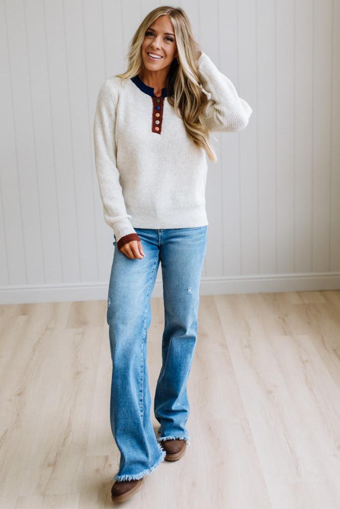 Blonde woman modeling an oat sweater with navy collar, mocha cuffs, and a mocha henlwy with multi color sweater covered buttons. Standing on a light wood floor with light backdrop.