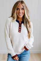 Blonde woman modeling an oat sweater with navy collar, mocha cuffs, and a mocha henlwy with multi color sweater covered buttons. Standing on a light wood floor with light backdrop.