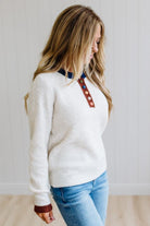 Blonde woman modeling an oat sweater with navy collar, mocha cuffs, and a mocha henlwy with multi color sweater covered buttons. Standing on a light wood floor with light backdrop.