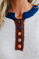 Blonde woman modeling an oat sweater with navy collar, mocha cuffs, and a mocha henlwy with multi color sweater covered buttons. Standing on a light wood floor with light backdrop.