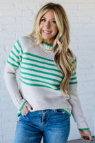 Woman wearing a striped sweater and jeans against a white brick wall