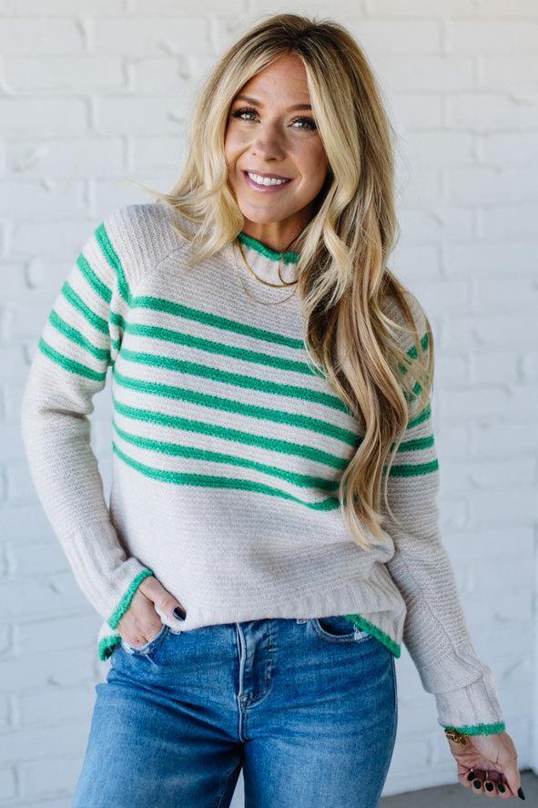 Woman wearing a striped sweater and jeans against a white brick wall