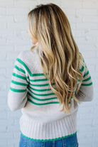 Person wearing a white sweater with green stripes against a white brick wall.