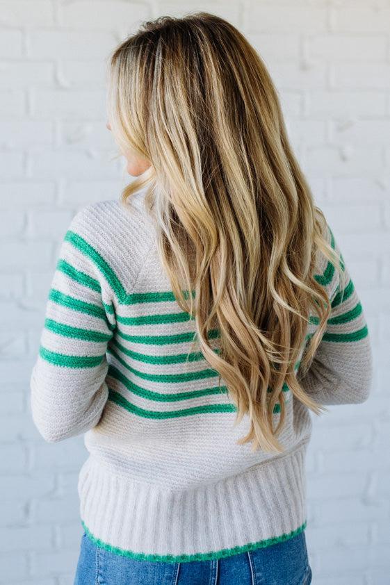 Person wearing a white sweater with green stripes against a white brick wall.