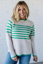 Woman wearing a gray and green striped sweater against a white brick wall.