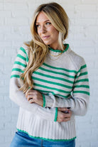 Woman wearing a green and white striped sweater against a white brick wall.
