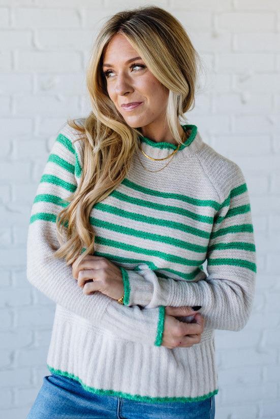 Woman wearing a green and white striped sweater against a white brick wall.