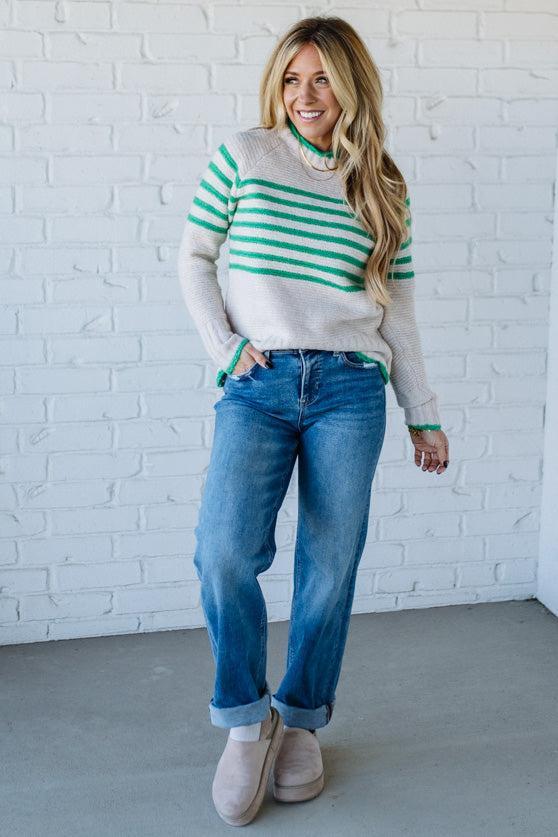Woman wearing a striped sweater, jeans, and UGG boots against a white brick wall.