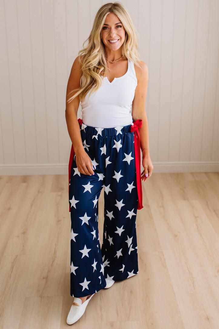 Woman wearing a white top and red, white, and blue star-patterned pants on a wooden floor.