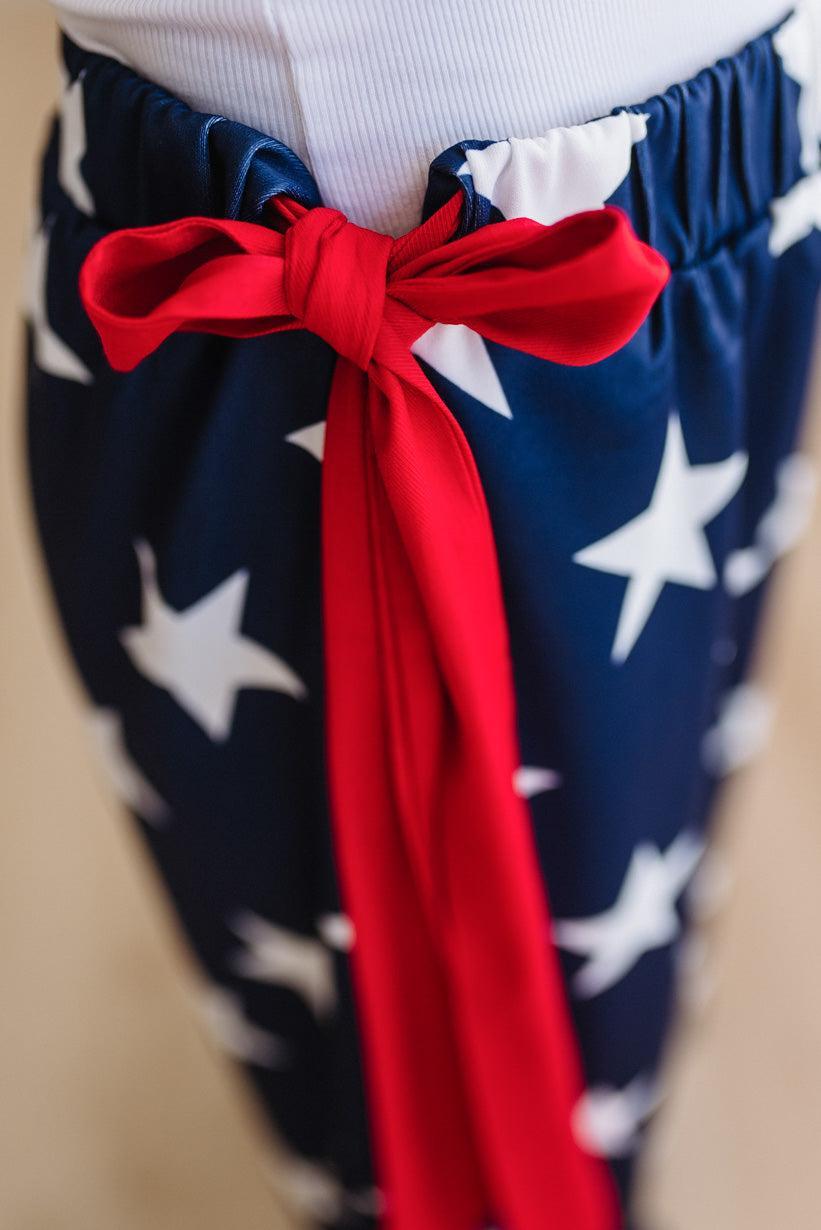 Navy blue pants with white star pattern and a red ribbon, worn over a white top.