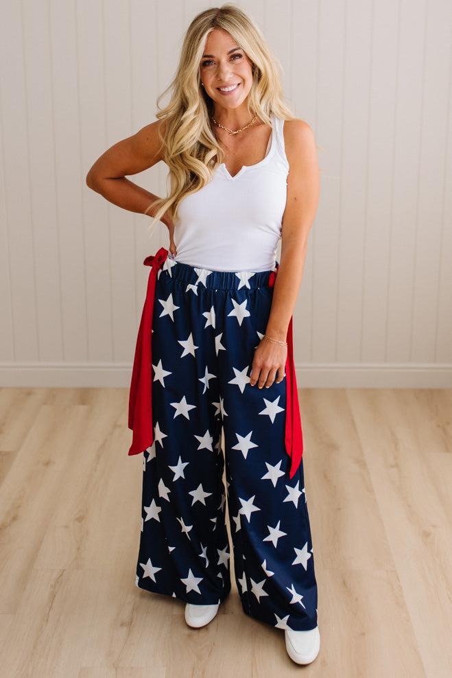 Woman wearing a white tank top and red, white, and blue star-patterned pants on a wooden floor.