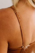 Close-up back view of a woman wearing a tan faux-suede spaghetti strap dress with a gold chain detail and a sparkly brown sequined hem.