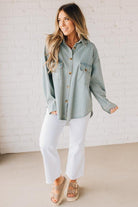 Blonde wearing a light blue denim oversized shirt with vertical white stripes and brown large buttons.