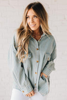 Blonde wearing a light blue denim oversized shirt with vertical white stripes and brown large buttons.