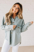 Blonde wearing a light blue denim oversized shirt with vertical white stripes and brown large buttons.