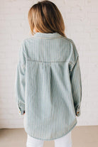 Blonde wearing a light blue denim oversized shirt with vertical white stripes and brown large buttons.