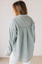 Blonde wearing a light blue denim oversized shirt with vertical white stripes and brown large buttons.