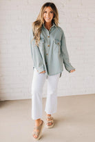 Blonde wearing a light blue denim oversized shirt with vertical white stripes and brown large buttons.