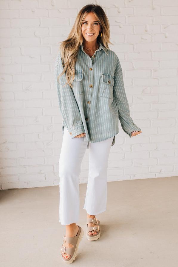 Blonde wearing a light blue denim oversized shirt with vertical white stripes and brown large buttons.